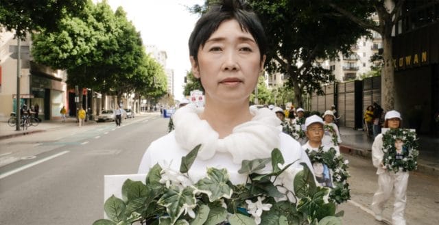 中国の労働収容所で殺害された妹を追悼する花輪を手にする王易非さん。王さんは同じ運命から逃れるために中国を脱出した。2016年、ロサンゼルスで行われたパレードで。
